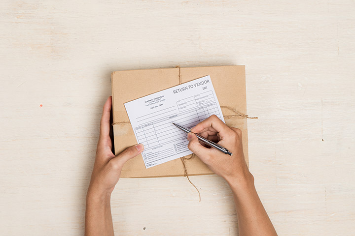 Image: A pair of hands filling out a return to vendor sheet on top of a package.