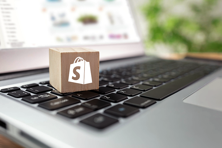 Image: A closeup of a block sitting on laptop with a white Shopify logo on the front.