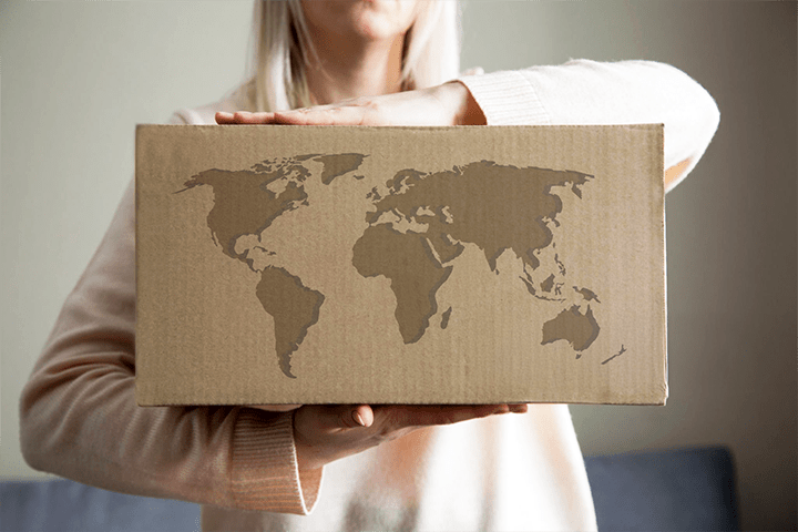 Image: Ecommerce shipper holding a package with a world map overlay on the front.
