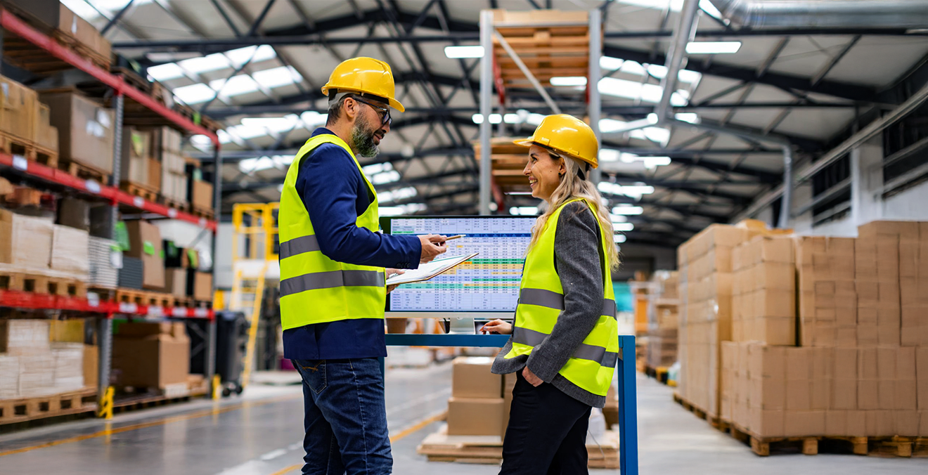 Image: Two warehouse workers strategizing logistics in front of a digital screen.