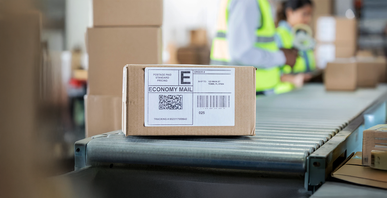 Image: A box with a shipping label sitting on a conveyor belt in a package warehouse.