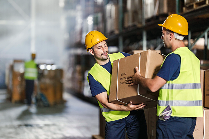 Image: Two warehouse workers carrying a package in a shipment warehouse.